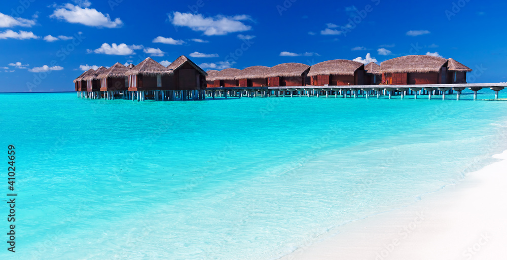 Overwater villas in blue tropical lagoon with white beach