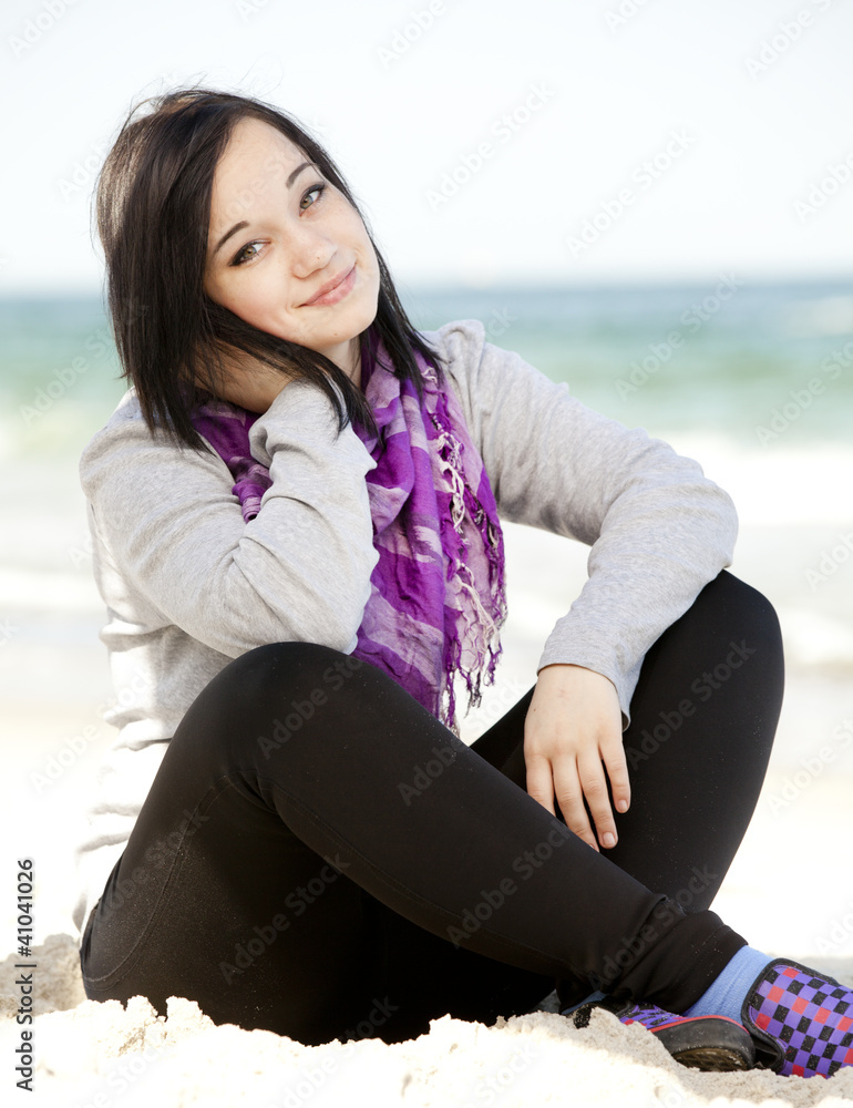 Funny teen girl sitting on the sand at the beach.