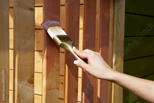woman's hand with a paint brush painting wooden terrace in pink