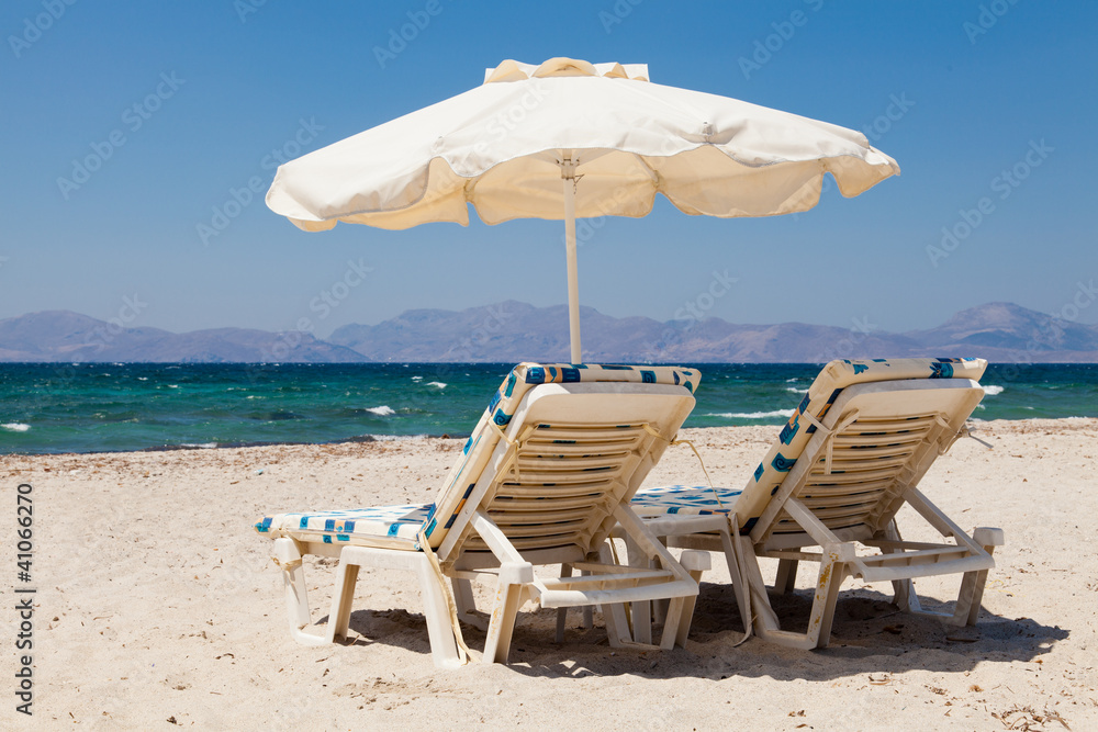 Deckchairs under parasol on sunny beach