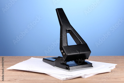 Black office hole punch with paper on blue background