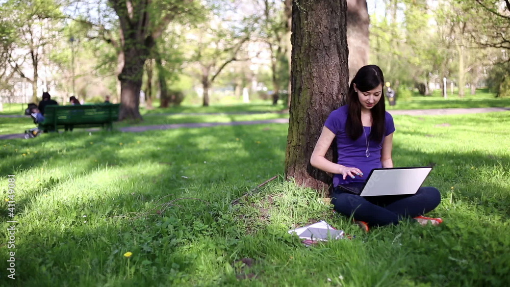 Happy female student with laptop relaxing in the park Happy female student with laptop relaxing in the park