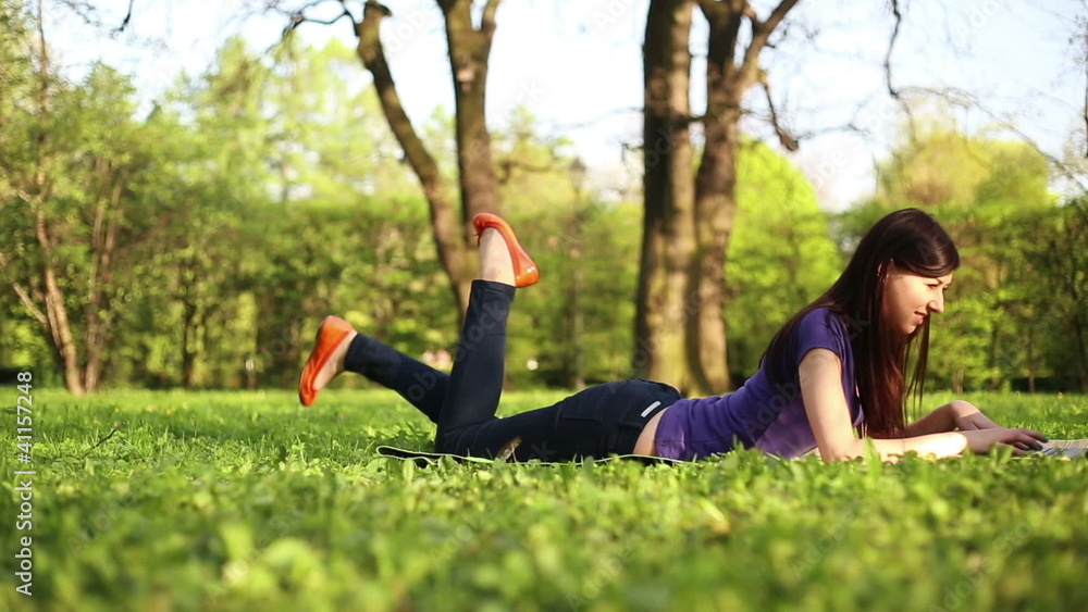 Young girl lying on grass with laptop in the park, dolly shot Young girl lying on grass with laptop in the park, dolly shot