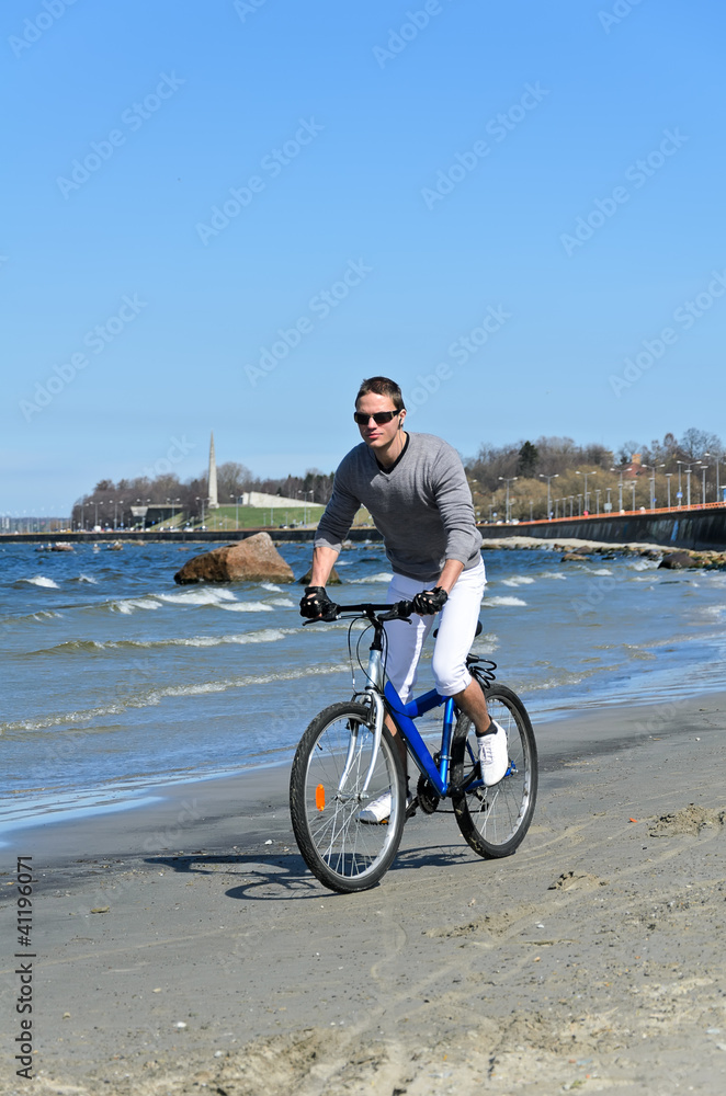 Fototapeta premium Portrait of handsome male riding a bicycle by the sea