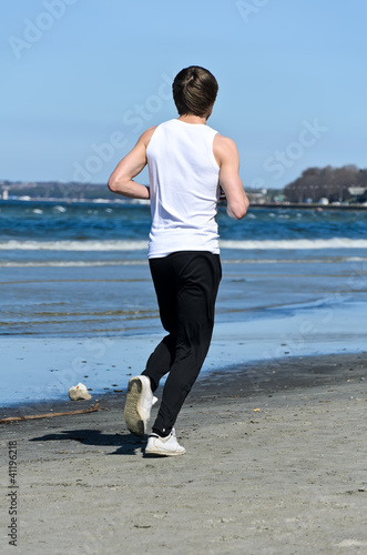 Fototapeta Naklejka Na Ścianę i Meble -  Athletic young male running on the beach. From the back