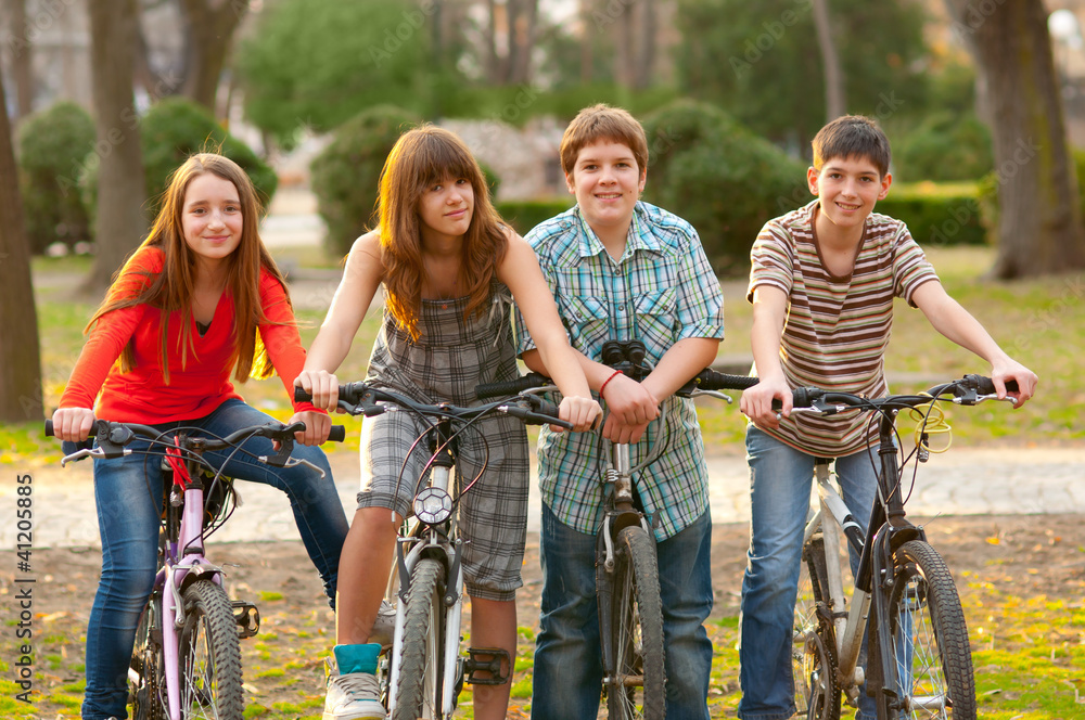 Four happy teenage friends riding bicycles in the park