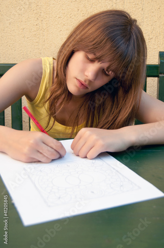 Cute teenage girl drawing ornaments on peace of white paper