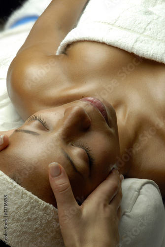 Joven mujer morena recibiendo masaje facial en un spa.
