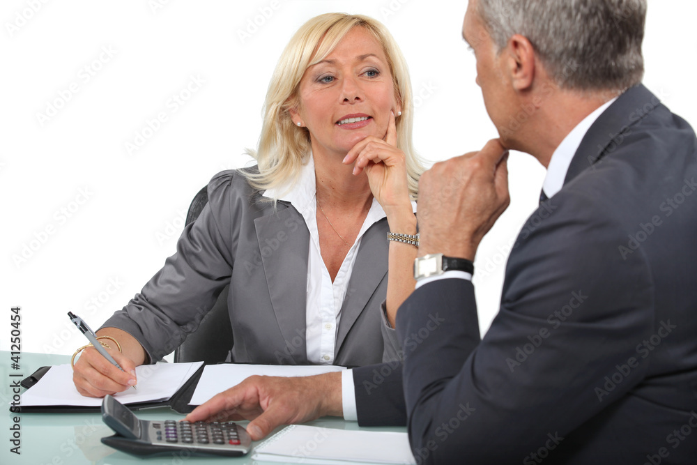 Mature business couple at a desk with a calculator Mature business couple at a desk with a calculator
