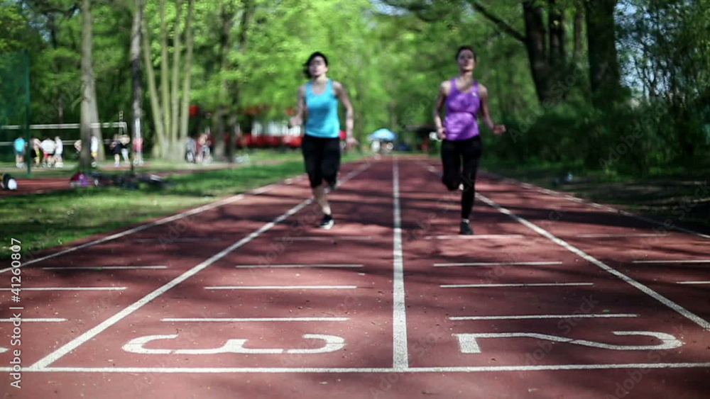Two women running on track lane, slow motion, dolly shot Two women running on track lane, slow motion, dolly shot