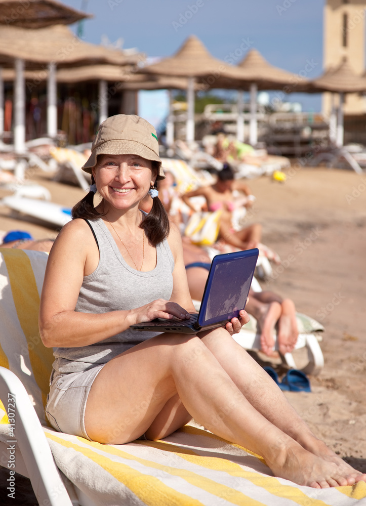 Happy woman sitting  with laptop at  beach
