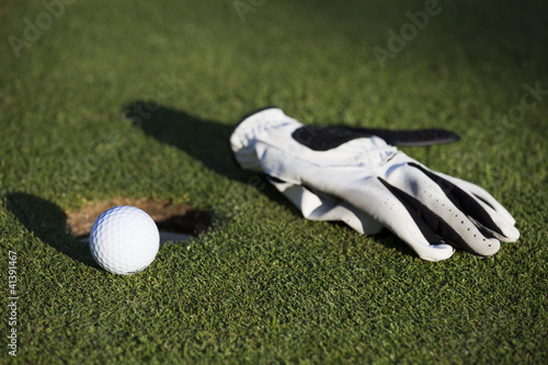 Balle et gant de golf près d'un trou