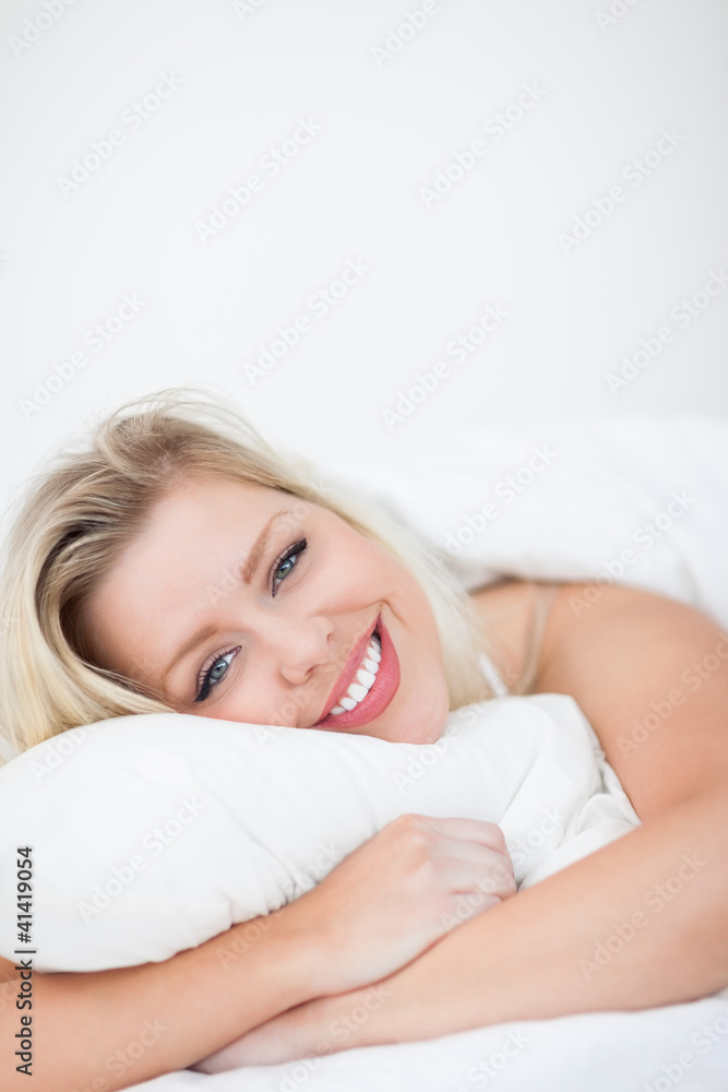 Young woman smiling while embracing a pillow Young woman smiling while embracing a pillow