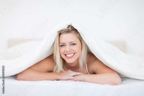 Young blonde woman lying under a duvet