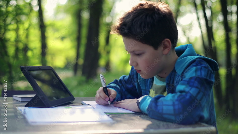 Young boy doing homework and using tablet computer in the park Young boy doing homework and using tablet computer in the park