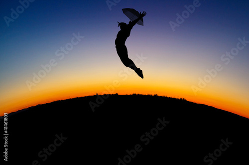 silhouetted girl jumps with umbrella in sunset
