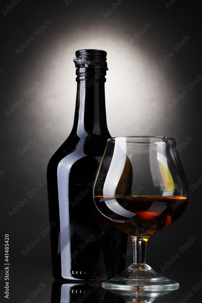 Glass of brandy and bottle on gray background Glass of brandy and bottle on gray background