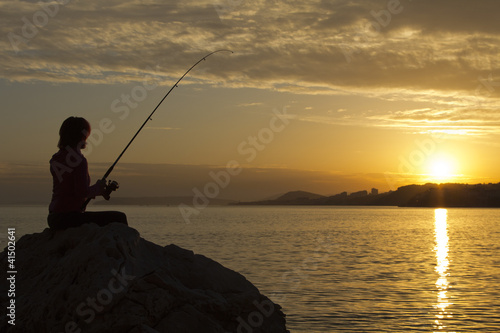 Happy girl fishes at sunset, near the sea at sunset