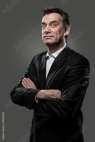 Handsome Middle Age Business Arms Folded Pulling Face on Grey