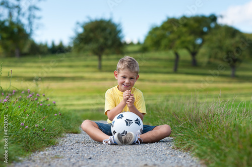 Junge mit Fußball sitzt auf einem Feldweg