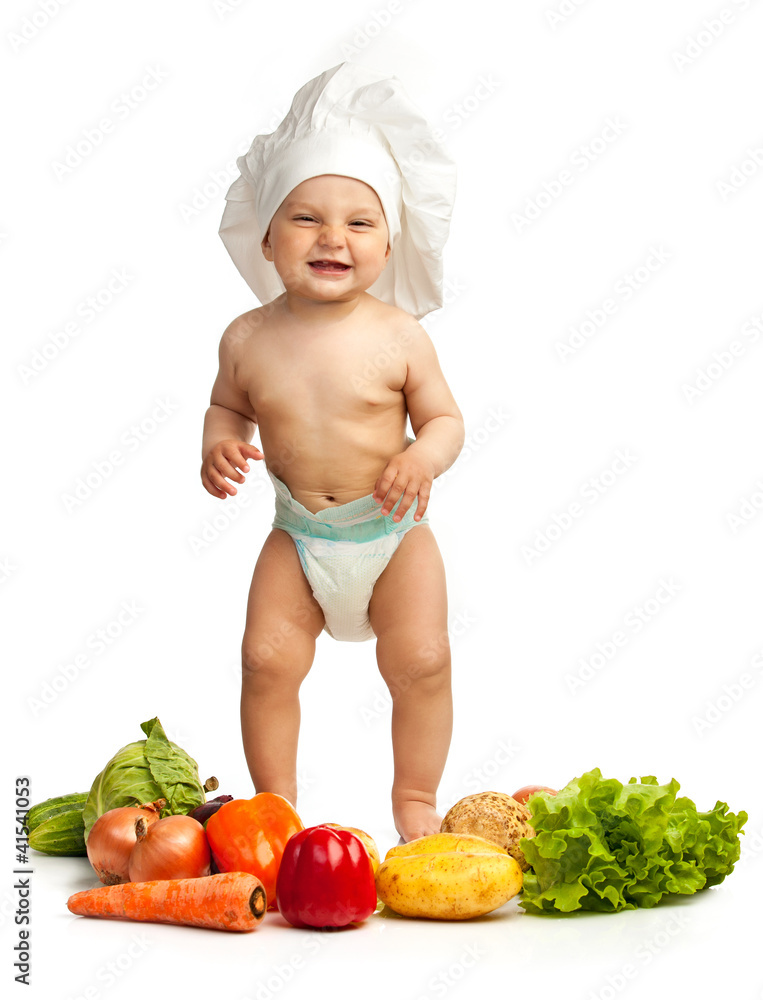 Little boy in chef's hat standing among fresh vegetables Little boy in chef's hat standing among fresh vegetables