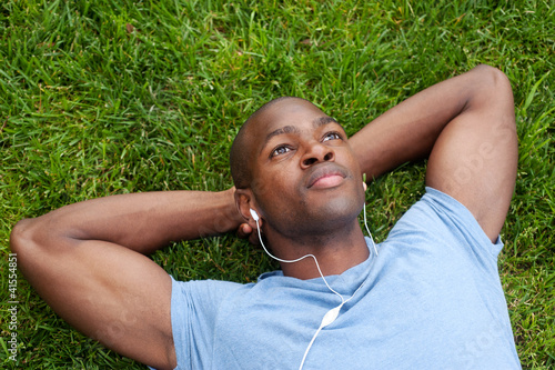 African American man lying in grass listening to music