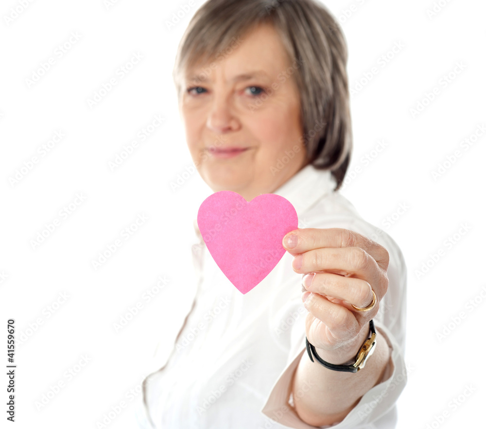 Focus on pink paper heart. Aged woman holding it Focus on pink paper heart. Aged woman holding it