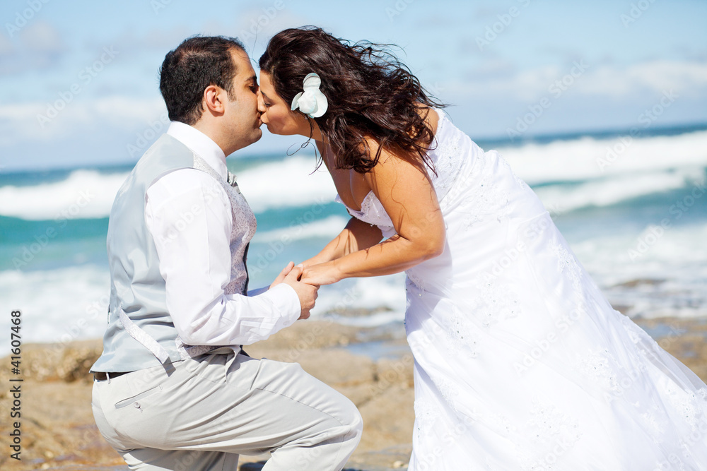 newlywed couple kissing on beach rocks