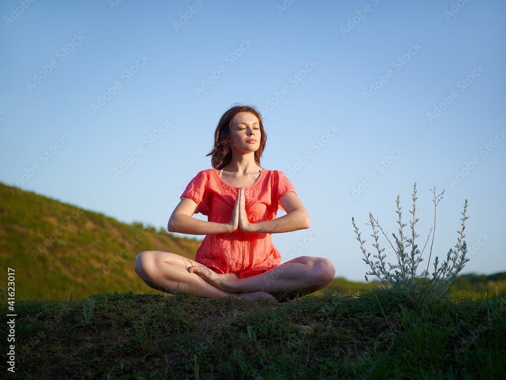 The young woman meditates on a green hill, in a lotus pose