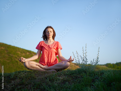 The young woman meditates on a green hill, in a lotus pose © Maxim Vlasenko