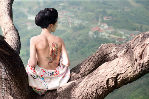 Woman with snake tattoo sitting on tree branch (Orig) photo