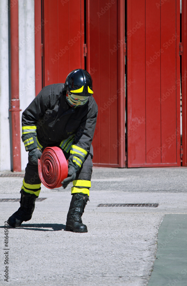 Fototapeta premium Fireman while unrolls a fire hose to extinguish the flames