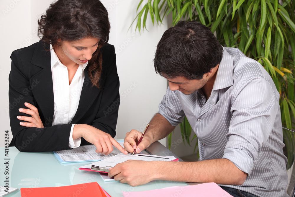 Businesswoman helping her client fill in paperwork Businesswoman helping her client fill in paperwork