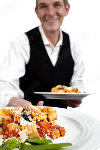 A waiter serves pasta. Focus on plate. Close-up.