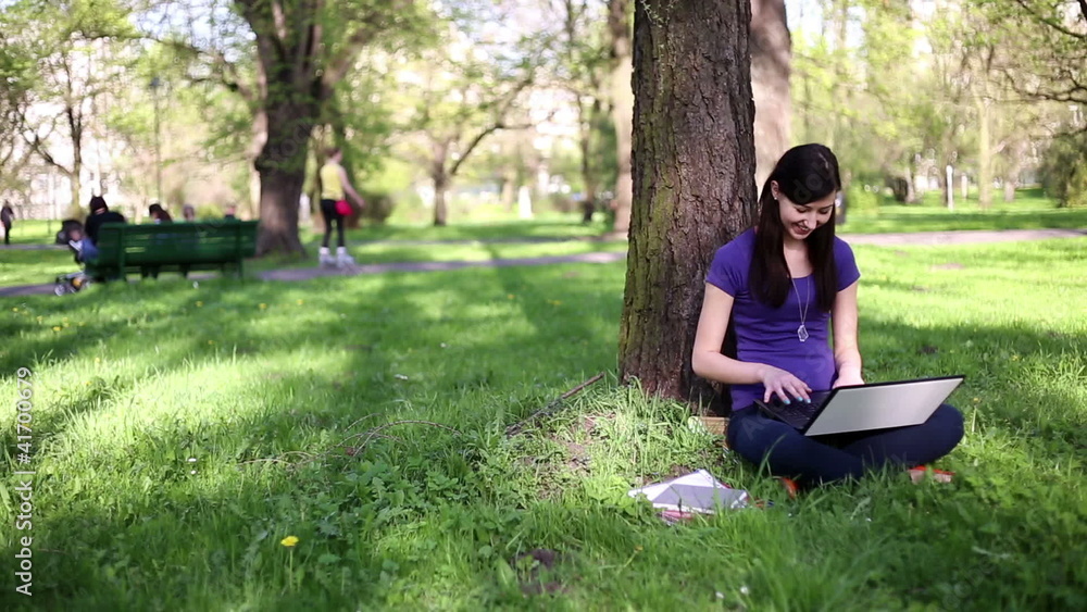 Young woman sitting in park with laptop, tracking shot Young woman sitting in park with laptop, tracking shot
