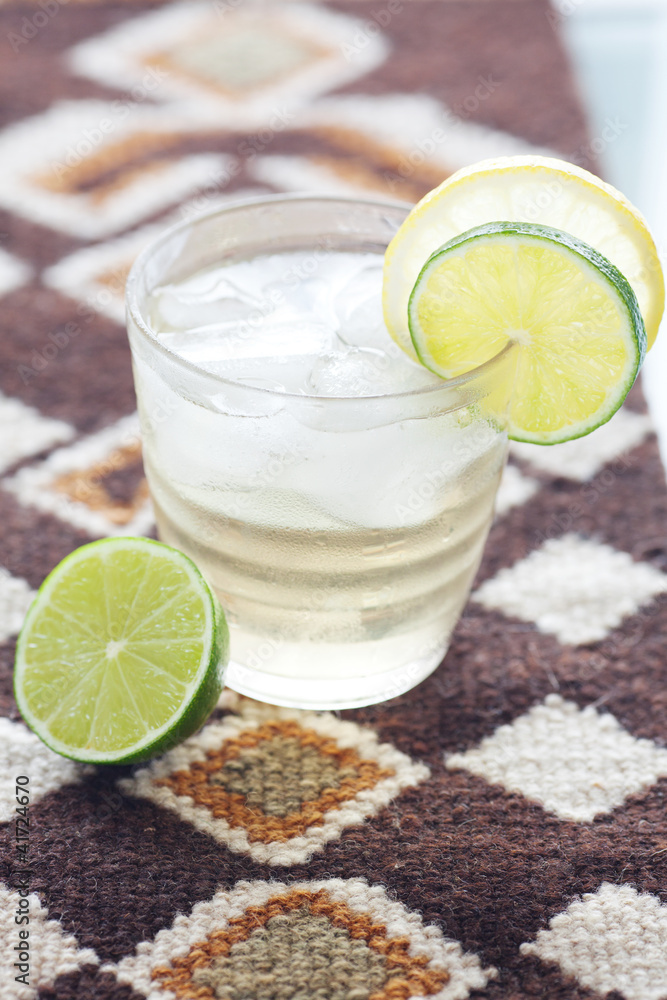 Fototapeta premium water with lemon and lime in a glass with ice on ethnic mat