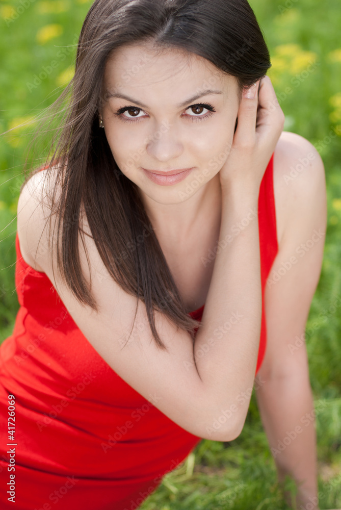 Young pretty woman in red dress sitting on green grass