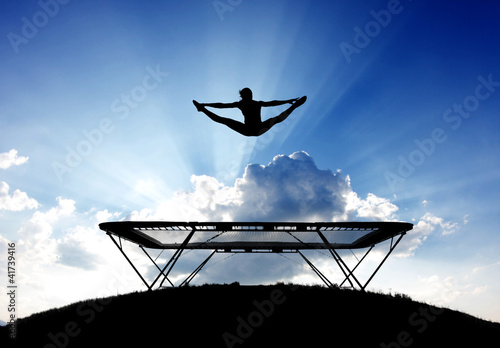 silhouette of female gymnast on trampoline in front of clouds