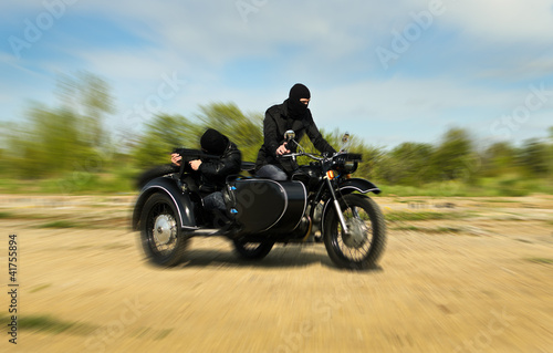 Two armed men riding a motorcycle with a sidecar. Motion blur.