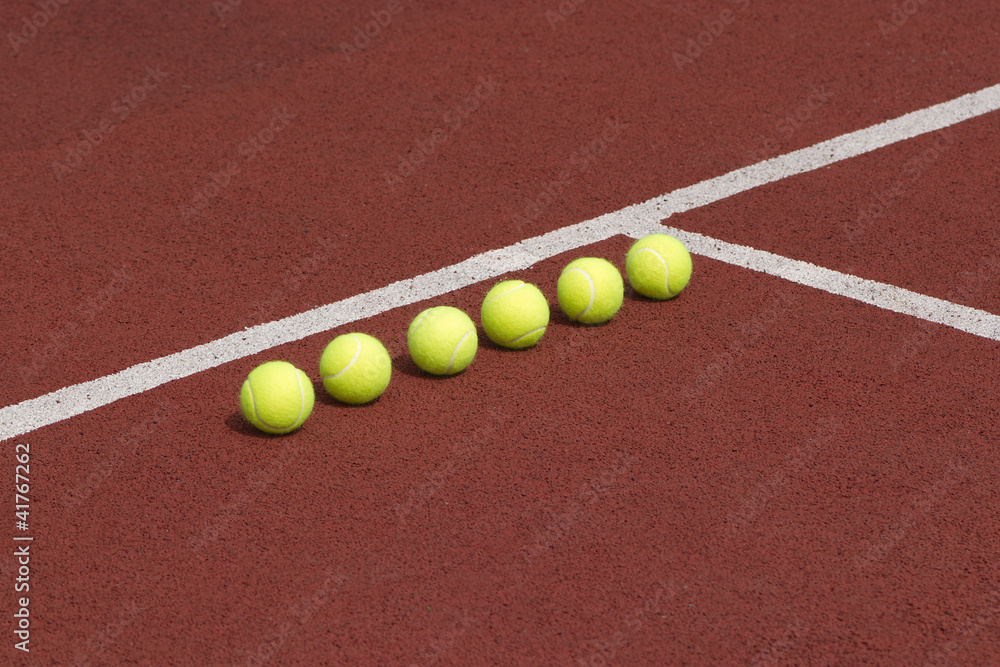 Line of six yellow tennis balls on court