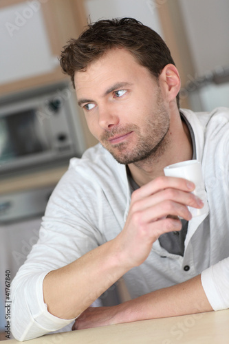 Portrait of handsome guy drinking coffee in home kitchen