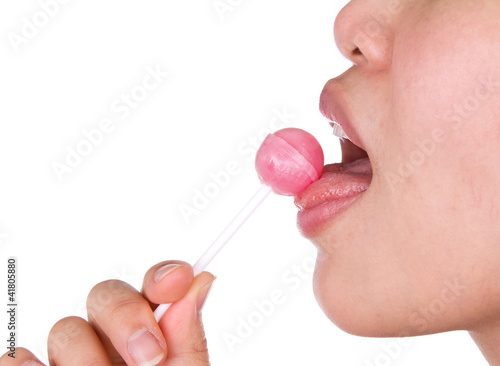 Woman licking a pink shiny lollipop on white background.