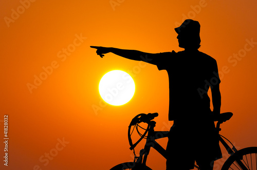 Silhouette of the bicycle rider against sun and orange sky