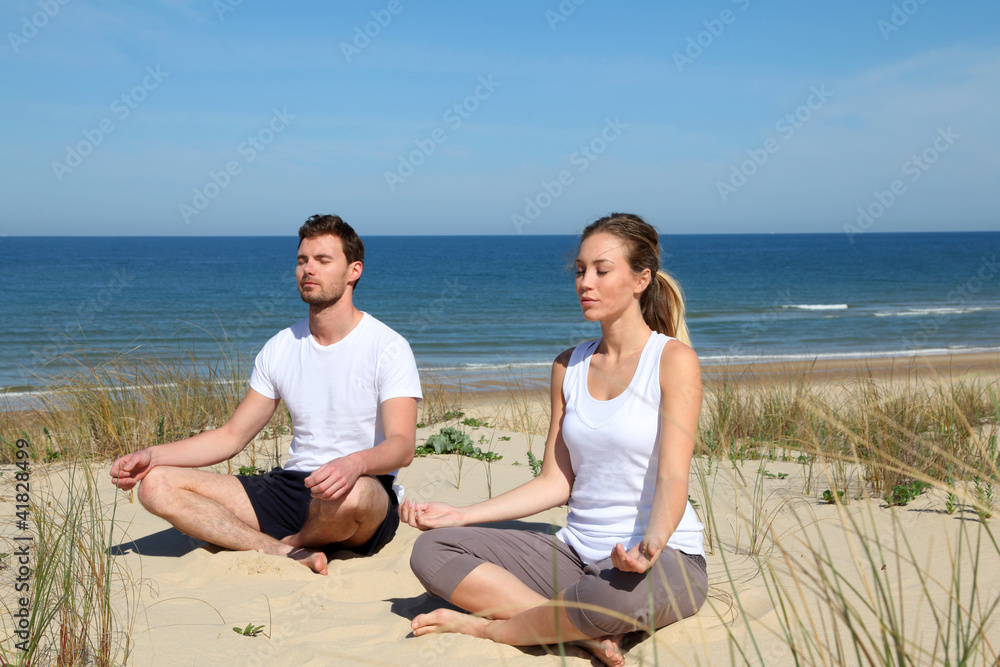 Couple doing yoga exercices on a sandy beach