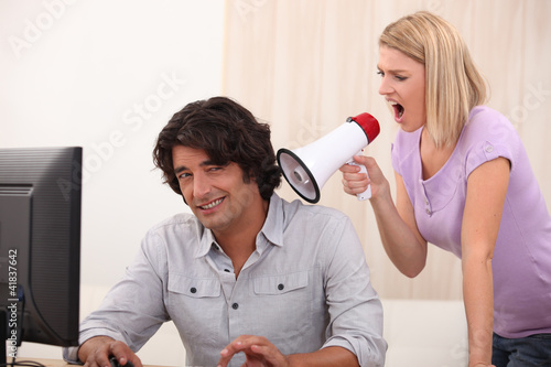 a man doing computer and a woman yelling on him with a megaphone photo