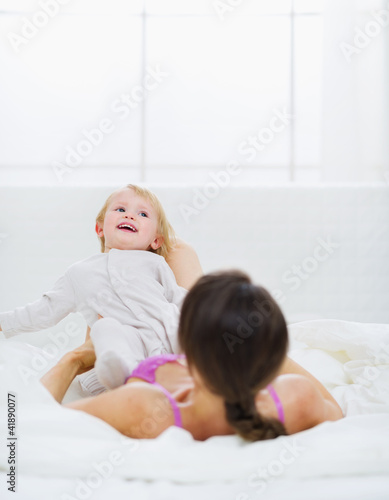 Mother playing with baby on bed