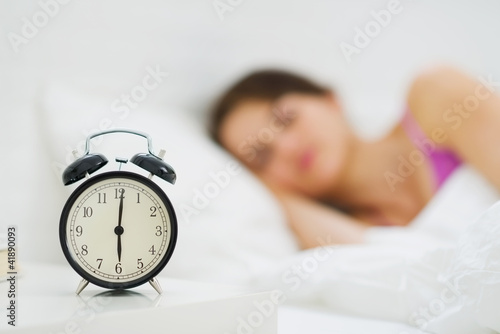 Alarm clock on table and woman sleeping in background photo