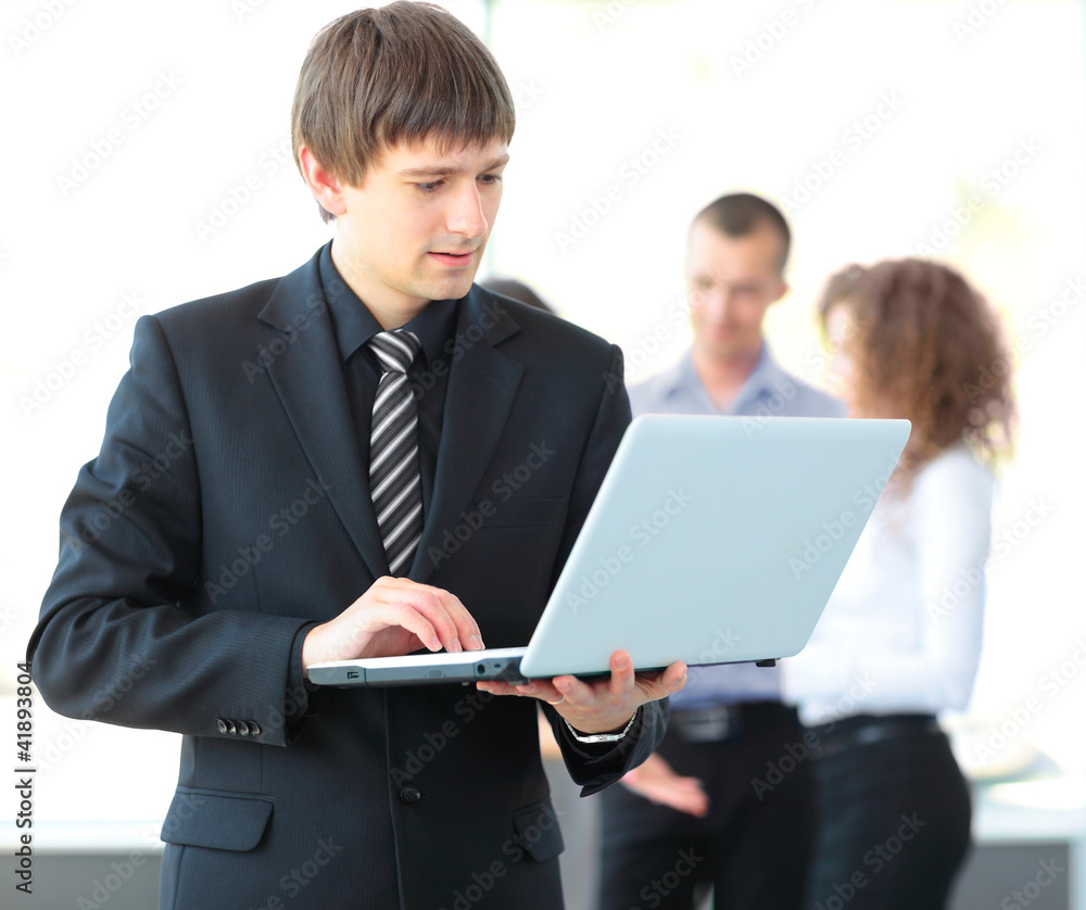 business man using laptop with colleagues in the background business man using laptop with colleagues in the background