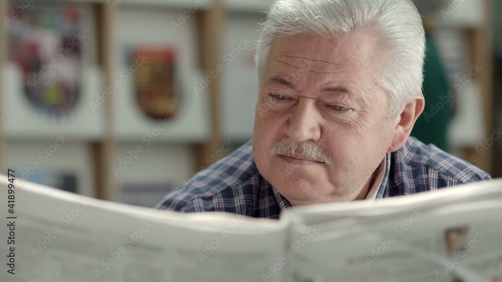 Senior man with mustache reading newspaper in library