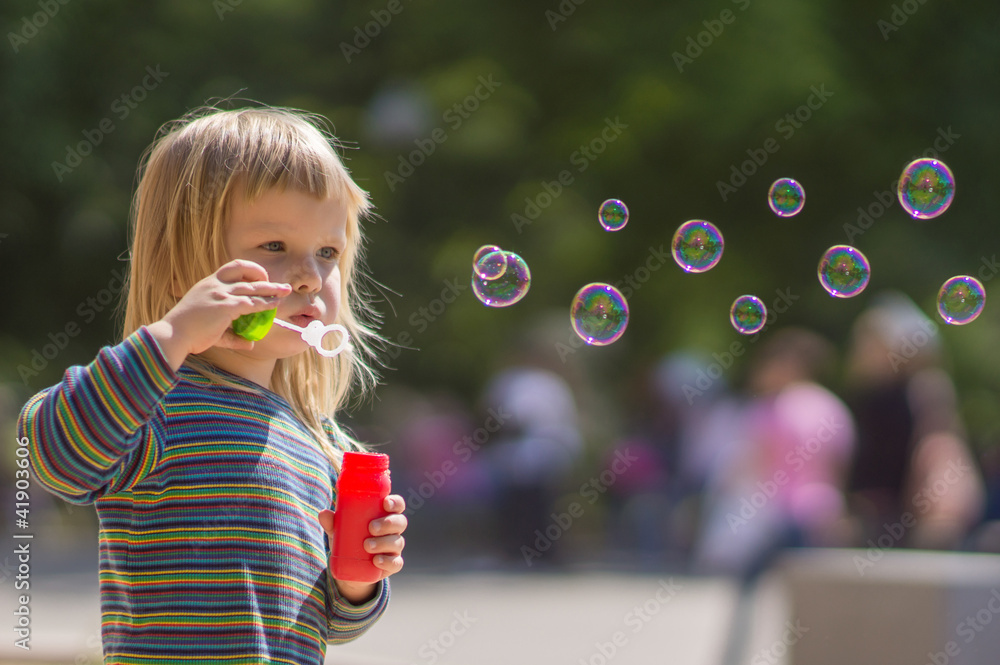 Adorable baby blow soap bubbles in park